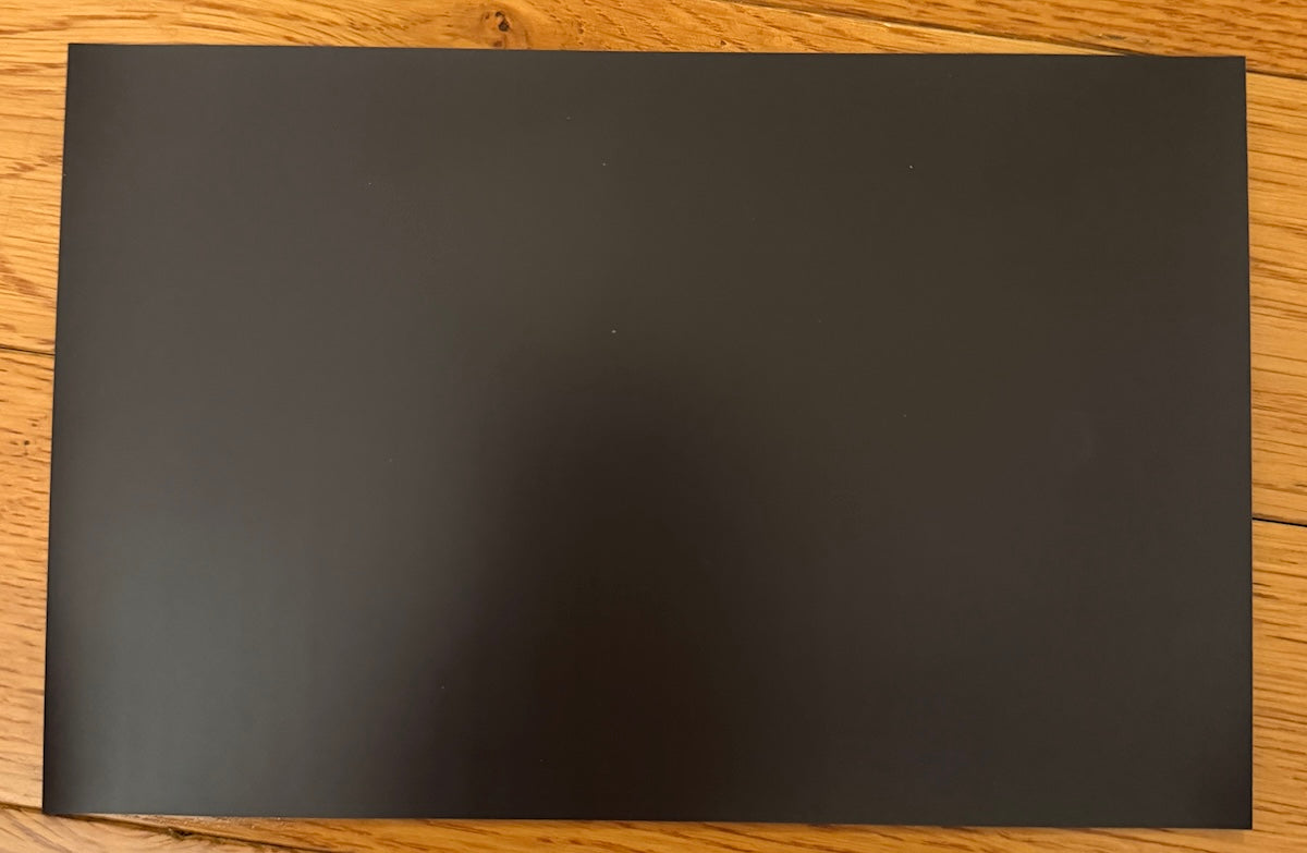 A plain black rectangular sheet or mat placed on a light brown wood surface.
