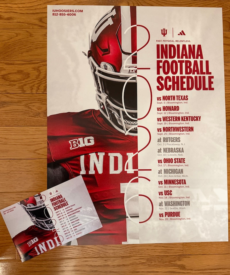 A printed football schedule poster for Indiana University, featuring a large red helmeted football player on a cream background with bold red text listing game opponents. A matching printed card is placed in front on a wood surface.